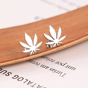 Polished silver cannabis leaf stud earrings displayed on a rustic wood and paper background