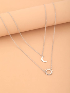 Detail of silver double-layer necklace with sun and moon pendants on a warm background