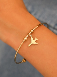 Macro detail of gold airplane charm on minimalist stainless steel open bangle bracelet