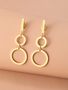 Detail of gold geometric earrings with dual hollow rings on a soft pink background