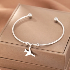 Minimalist stainless steel open bangle featuring an airplane pendant on a champagne jewelry box