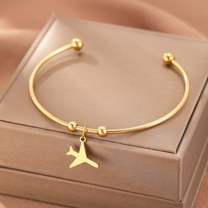 Gold stainless steel open bangle with a polished airplane charm on a jewelry box