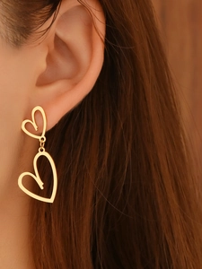 Gros plan de boucles d'oreilles double cœur doré portées avec finition polie