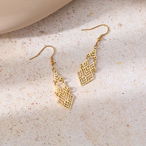 Detailed view of bohemian gold geometric drop earrings on a textured stone surface