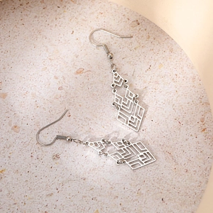 Macro shot of silver geometric hollow rhombus earrings on a stone textured surface