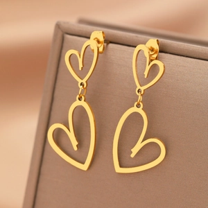 Boucles d'oreilles cœur en acier doré suspendues sur un écrin à bijoux marron texturé