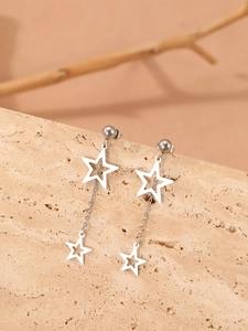 Détail de boucles d'oreilles étoiles en acier argenté suspendues sur une pierre beige
