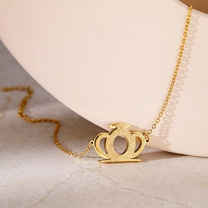 Détail du pendentif couronne en or mat ajouré sur une chaîne en acier inoxydable doré