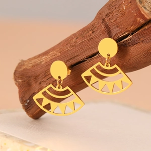 Macro detail of gold fan-shaped hollow earrings with geometric pattern on wood