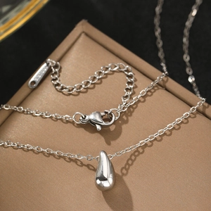 Collier pendentif goutte d'eau en acier inoxydable argenté posé sur un coffret à bijoux