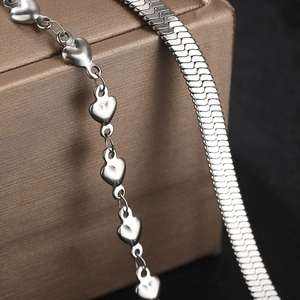 Close-up of polished silver heart link chain and sleek flat herringbone snake necklace