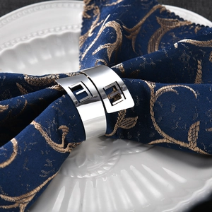 Polished silver metal napkin ring with geometric square design on a blue napkin