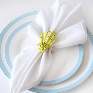 Detailed view of neon green skeleton hand napkin ring with gold band on white plate