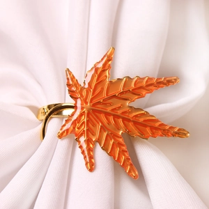Golden maple leaf napkin ring with vibrant orange enamel finish on white cloth