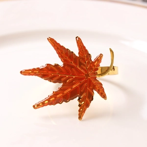 Golden maple leaf napkin ring with orange enamel on a white ceramic plate for table decor