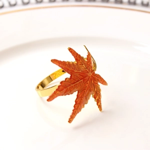 Golden maple leaf napkin ring with orange enamel finish on white porcelain plate