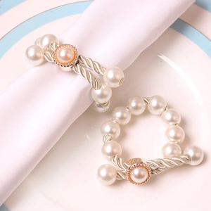 Elegant handmade pearl napkin rings with pink crystal bow accents on white ceramic plate