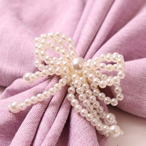 Elegant pearl bow napkin ring with white faux pearls on a textured purple fabric background