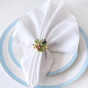 Detail of a coral napkin ring with colorful fish charms on a white folded napkin
