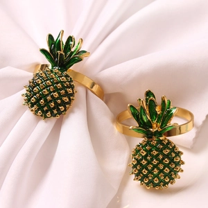 Ronds de serviette ananas dorés avec détails en émail vert sur tissu blanc