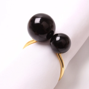Servilletero dorado en forma de U con perlas negras sobre rollo de tela blanca