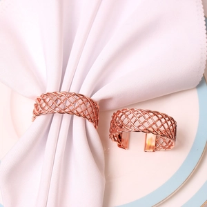Rose gold spiral mesh napkin rings set of two shown on a white ceramic plate