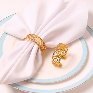 Handwoven golden metal napkin rings with hollow mesh design on a white dinner plate