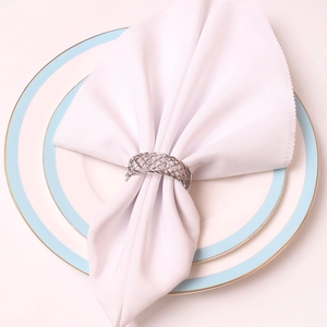 Close-up of a silver woven mesh napkin ring on a white cloth and elegant blue plate