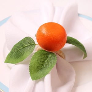 Macro shot of realistic orange napkin ring with green leaves on a white linen cloth