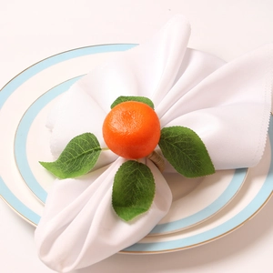 Realistic orange fruit napkin ring with green leaves on white napkin and ceramic tray