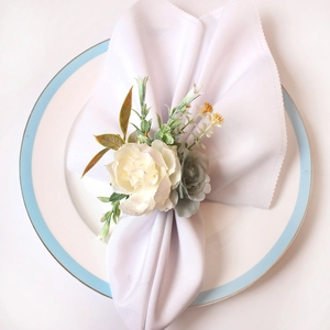 Eleganter Serviettenring mit weißen und blauen künstlichen Rosen auf einem weißen Teller