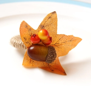 Autumn maple leaf and berry napkin ring with twine loop on a white plate for holiday table decor