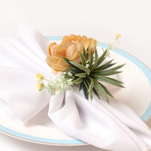 Champagne artificial flower napkin ring with green succulent leaves on a white fabric napkin