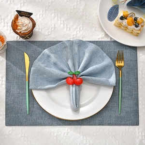 Detail of wooden cherry napkin ring with green leaves on blue fabric and grey placemat