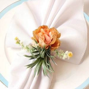 Rustic floral napkin ring with orange-pink faux rose and green leaves on a white plate