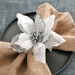 Detail of white poinsettia flower napkin ring with silver glitter and berries on a plate
