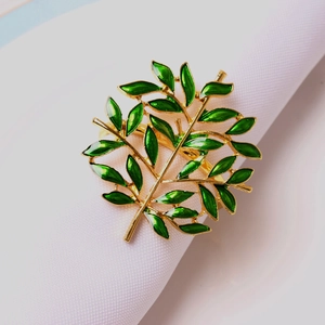 Close-up of golden branch napkin ring with green enamel leaves on white cloth