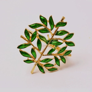 Detailed close-up of golden tree napkin ring with green enamel leaves on a plain background