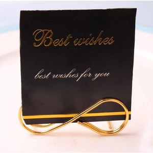 Close-up of golden infinity-shaped metal place card holder on a white ceramic plate