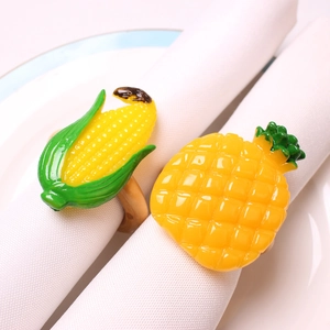 Dettaglio di portatovaglioli artificiali con mais e ananas su tessuto bianco e piatto ceramica