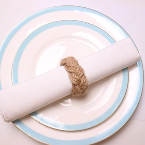 Detail of handmade braided jute rope napkin ring around a white cloth napkin