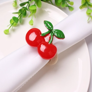 Detail of cherry napkin ring with red resin cherries and green leaves on white linen