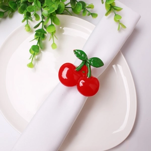 Close-up of artificial cherry napkin ring with red fruit and green leaves on white linen