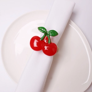 Detailed close-up of a red cherry napkin ring with green leaves on a white linen napkin