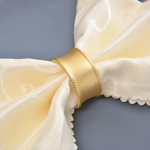 Elegant gold beaded napkin ring with matte metal finish on a luxury beige cloth