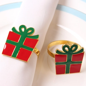 Detail view of a gold gift box napkin ring with red and green enamel on white fabric