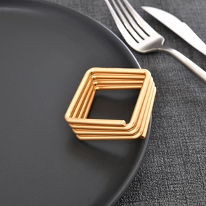 Modern square gold metal wire napkin rings set displayed on a dark ceramic dinner plate