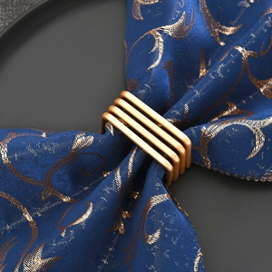Square gold wire wrapped metal napkin ring set on a navy patterned cloth napkin