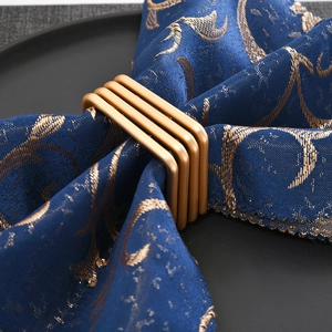 Square gold wire mesh napkin ring set with four connected metal bands on a dark plate