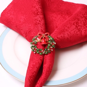 Servilletero corona de Navidad con lazo rojo y cascabeles sobre un plato blanco